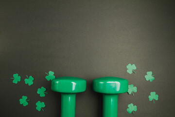 Green dumbbells and clover for St. Patrick's Day. Composition on black backdrop with copyspace.