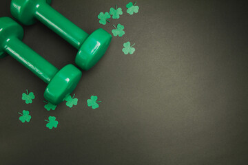 Green dumbbells and clover for St. Patrick's Day. Composition on black backdrop with copyspace.