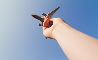 Hand holding a toy plane. Flying airplane model against clear blue sky.