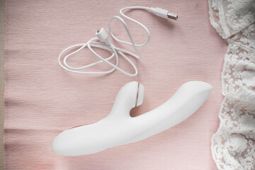 white silicone vibrator with vacuum mode on pink lace background with magnetic charging