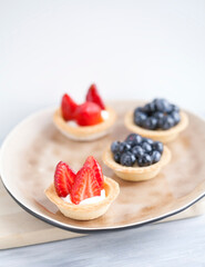 cake with cheese cream and fresh berries and wild berries on a beige plate on a wooden light background. Idea for culinary recipes and desserts. Perfect party individual fresh fruit dessert.