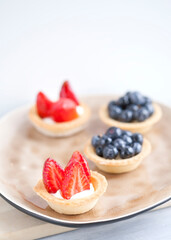 cake with cheese cream and fresh berries and wild berries on a beige plate on a wooden light background. Idea for culinary recipes and desserts. Perfect party individual fresh fruit dessert.