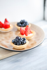 cake with cheese cream and fresh strawberries and wild berries on a beige plate on a wooden light background. Idea for culinary recipes and desserts. Perfect party individual fresh fruit dessert.