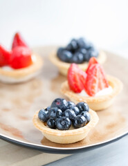 cake with cheese cream and fresh berries and wild berries on a beige plate on a wooden light background. Idea for culinary recipes and desserts. Perfect party individual fresh fruit dessert.