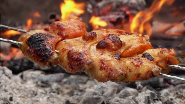Delicious chicken wings on the skewers are flipped above the open fire outdoors in rapid 