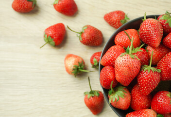 The bright red strawberries are ripe in a cup, black, placed on a wooden table, taken up close, and with a stem, green leaves, brought together.