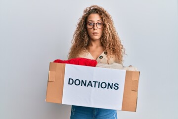 Beautiful caucasian teenager girl volunteer holding donations box clueless and confused expression....