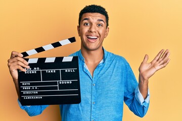 Young arab man holding video film clapboard celebrating achievement with happy smile and winner...