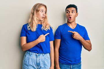 Young interracial couple wearing casual clothes surprised pointing with finger to the side, open mouth amazed expression.
