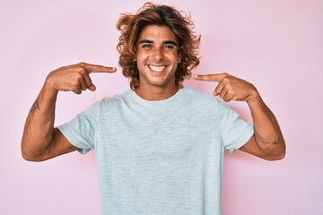 Young hispanic man wearing casual clothes smiling cheerful showing and pointing with fingers teeth...