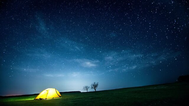 Glowing camping tent in the night mountains under the twinkling starry sky