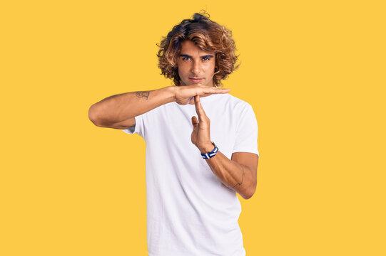 Young hispanic man wearing casual white tshirt doing time out gesture with hands, frustrated and serious face