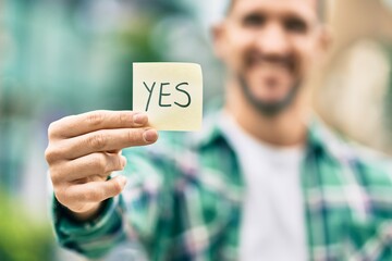 Young caucasian man smiling happy holding yes reminder papaer at the city.