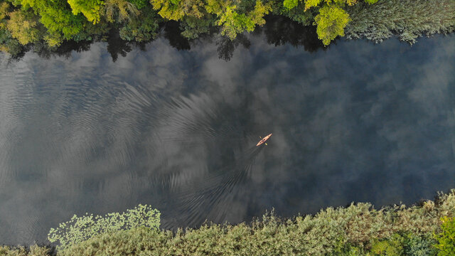 Top aerial view of the river along which a small orange kayak floats. Green trees grow on the shore. Ukraine, Europe