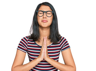 Beautiful asian young woman wearing casual clothes and glasses begging and praying with hands...