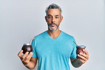Middle age grey-haired man drinking mate infusion relaxed with serious expression on face. simple...