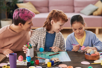 Obraz premium Mother with her children sitting at the table and painting eggs with crayons they preparing for Easter