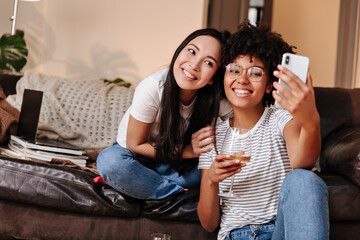 Photo taken at home of young girls relaxed sitting on large sofa surrounded by many books