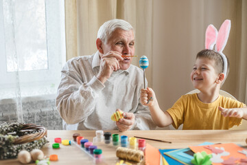 Happy elderly man grandfather preparing for Easter with grandson. Portrait of smiling boy with bunny ears painted  colored eggs for Easter