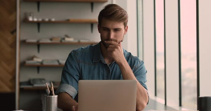 Focused young motivated man working on computer at home or office, stuck with difficult ask, thinking on problem solution, analyzing statistics data preparing electronic report, using software app.