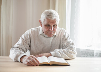 senior man praying, reading  an old Bible in his hands.