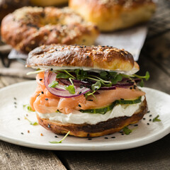 Smoked salmon bagels sandwich with soft cheese and micro greens on a cutting board.