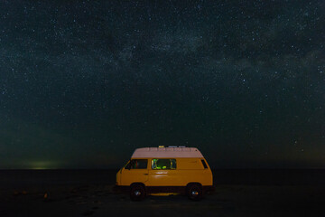 Fototapeta na wymiar Yellow vintage camper van at night parking under the starry sky.