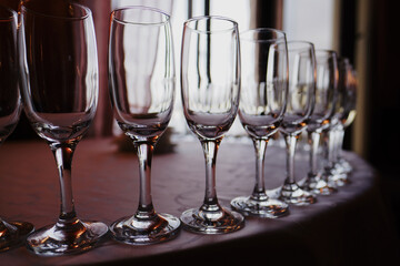 Champagne glasses stand in a semicircle in a row on a table covered with a light tablecloth, gloomy lighting, selective sharpness of the image and blurred