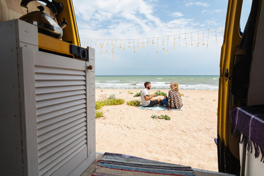 Young couple travelling by campervan along the seaside and chilling out at the beach