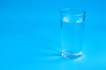 A glass of water on a blue background. The sun's rays are reflected in the water and on the background.