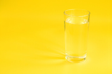 A glass of water on a yellow background. The sun's rays are reflected in the water and on the background.