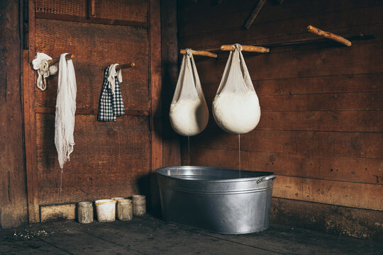 Still life with farmer cheese draining in cheesecloth above buckets on rustic wooden background