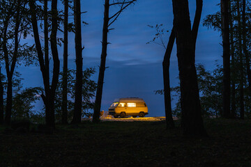 Yellow vintage camper van parked in the forest at night. Camping in the wild nature.