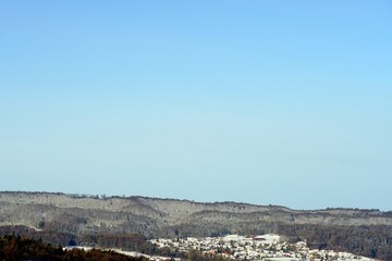 Fototapeta premium Winter landscape with copy space. A village surrounded by woodland covered with snow. Copy space in the sky above the trees. 