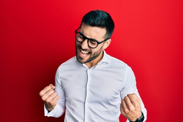 Young hispanic businessman wearing shirt and glasses excited for success with arms raised and eyes closed celebrating victory smiling. winner concept.