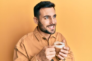 Handsome hispanic man enjoying a cup of coffee over yellow background