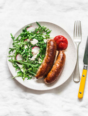 Fried pork sausages and salad with arugula, radish and mustard, yogurt dressing on a light background, top view