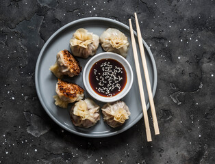 Pork wontons fried with sesame seeds and soy sauce on a dark background, top view