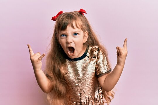 Little caucasian girl kid wearing festive sequins dress shouting with crazy expression doing rock symbol with hands up. music star. heavy concept.