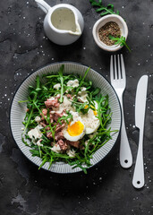 Salad with arugula, canned tuna, boiled egg and yogurt, mustard dressing on a dark background, top view