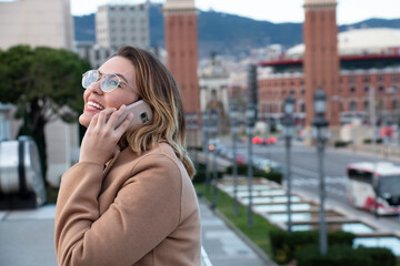 Young blonde woman with glasses laughs talking on the mobile in the city