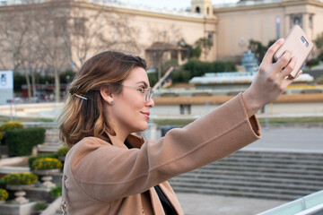 Young blonde woman with glasses takes selfie in the city