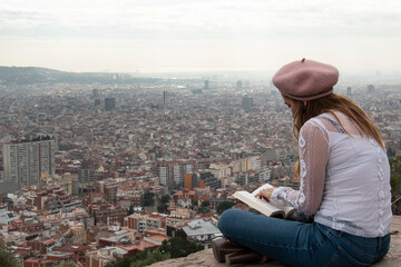 Woman quietly reads a book from a viewpoint in the city of Barcelona - obrazy, fototapety, plakaty