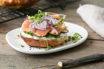 Smoked salmon bagels sandwich with soft cheese and micro greens on a cutting board.
