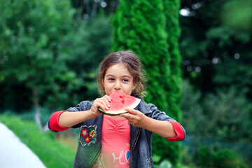 Little pretty girl eating a juicy watermelon in the garden. Children eat fruit outdoors. Healthy food for children.