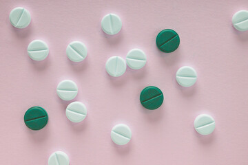 White and green pills lie on a sheet of pink paper. Close up. Light background or backdrop on the theme of medicine, health care, drugs, pharmacology. Tablets of different colors. View from above