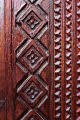 Close up ancient arabic carved pattern with rhombuses at wooden polished door, brown red vintage background 