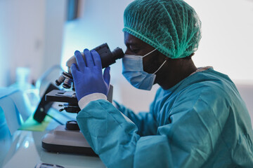 African man looking in microscope working inside hospital laboratory - Coronavirus outbreak