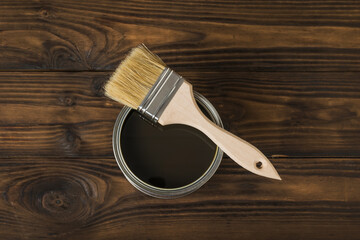 Brush on an open jar with a tinting composition on a wooden background.