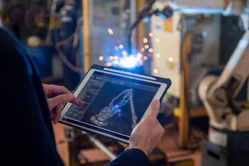Manager industrial engineer using tablet check and control automation robot arms machine for build a part of product.